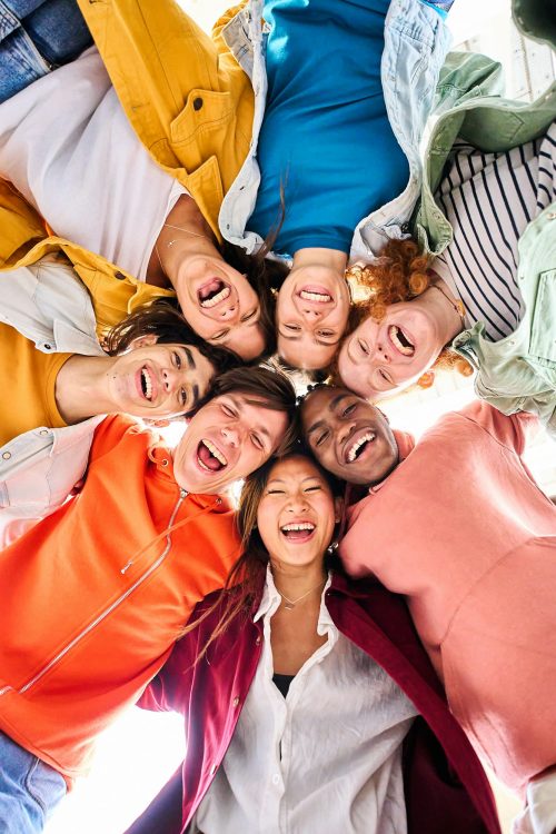 Vertical large multiracial group of smiling young people standing hugging looking at camera.